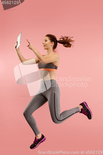 Image of Image of young woman over blue background using laptop computer or tablet gadget while jumping.