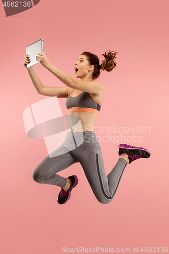 Image of Image of young woman over blue background using laptop computer or tablet gadget while jumping.