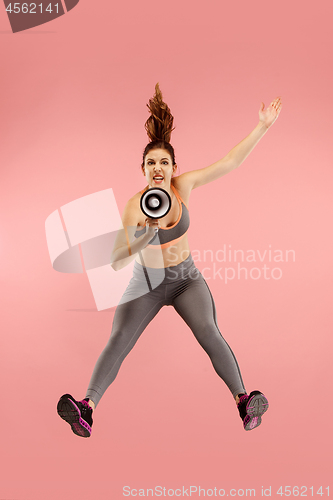 Image of Beautiful young woman jumping with megaphone isolated over red background