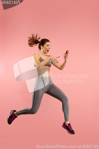 Image of Full length of pretty young woman with mobile phone while jumping