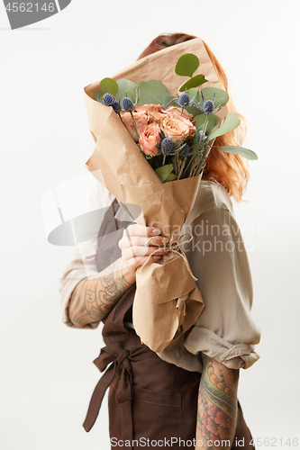 Image of Girl with red hair hide her face big fresh bunch from natural roses and green leaves on a light background. Copy space. Congratulation card.