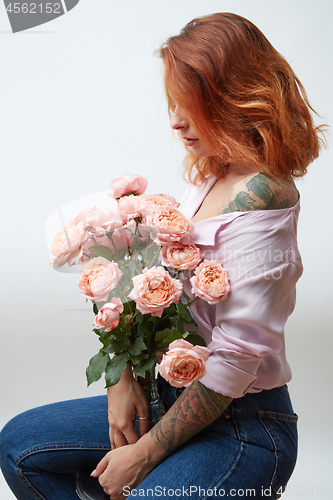 Image of A vase with a bouquet of pink roses is being held by a girl with a tattoo around a gray background with space for text. Present