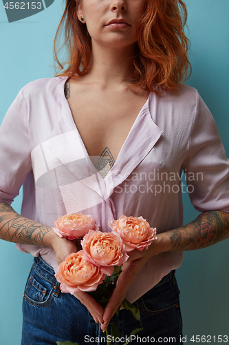 Image of Sexy girl with tattoo holding a bouquet of pink roses on a blue background with copy space. Creative layout for postcards