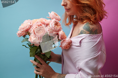 Image of Gentle pink roses in the hands of a girl with a tattoo on a double pink blue background with copy space for text. Birthday present