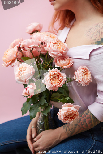 Image of A glass vase with delicate pink roses holds a girl with a tattoo around a pink background with space for text. Mothers Day
