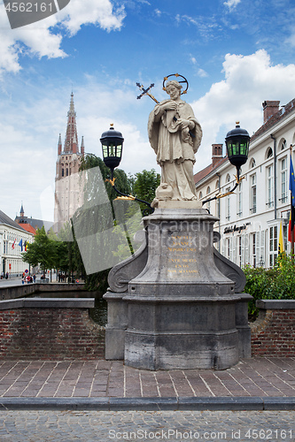 Image of Bruges, Belgium - August 16, 2013: Statue of Johannes Nepomucenus and the church tower against the blue sky in Bruges