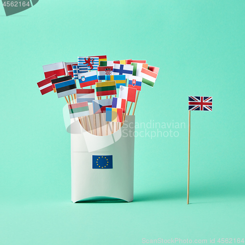 Image of Different paper flags in a cardboard box with an EU sign and flag of Britain aside on green background with copy space. The exit of Britain from the EU