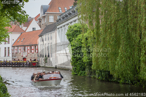 Image of Bruges, Belgium - May 17, 2012: Old houses on the water channel, with trees and a floating motor boat on a spring day.