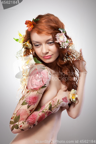Image of Beautiful red-haired girl with tattoo adorned with flowers on a gray background with copy space. Spring concept