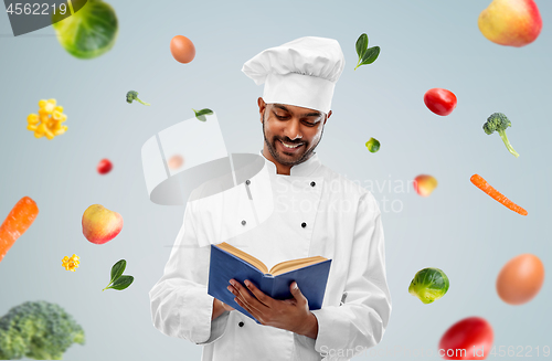 Image of happy indian chef reading cookbook over vegetables