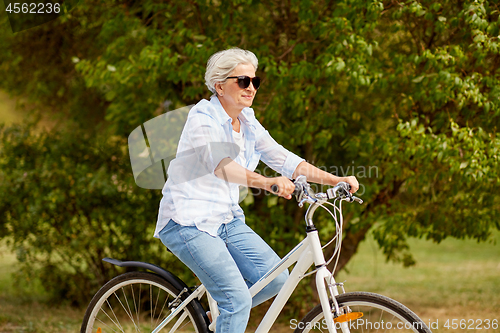 Image of happy senior woman riding bicycle at summer park