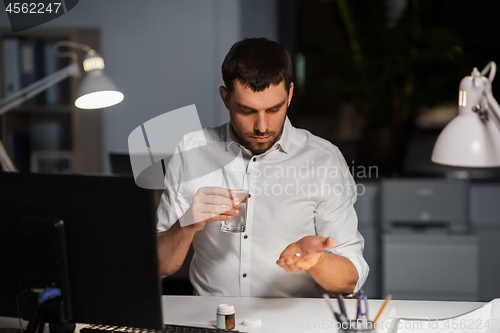 Image of businessman taking medicine pills at night office