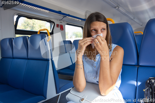 Image of A cold girl blows her nose in a scarf in an electric train car