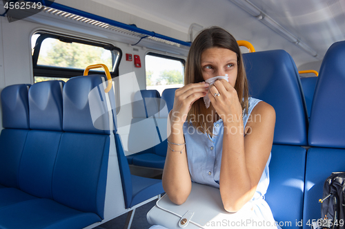 Image of A cold girl blows her nose in a scarf in an electric train car