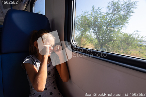 Image of A girl rubs her eyes from the sun in an electric train car