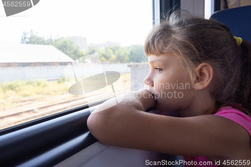 Image of A girl of eight years looks out the window in an electric train