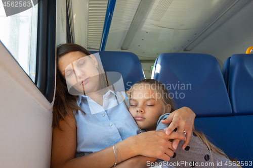 Image of Mom and daughter sleep in a seated carriage of an electric train