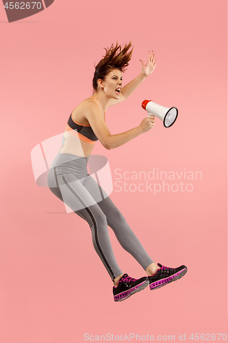 Image of Beautiful young woman jumping with megaphone isolated over red background