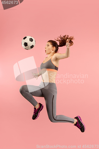 Image of Forward to the victory.The young woman as soccer football player jumping and kicking the ball at studio on a red