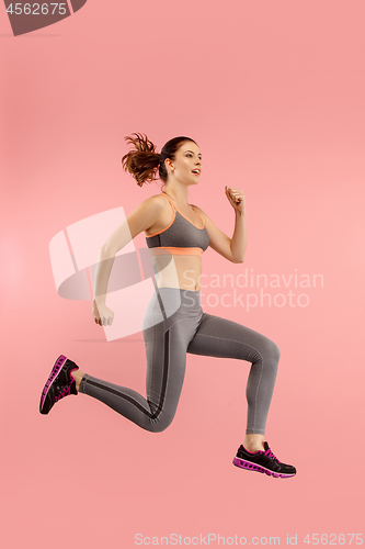 Image of Freedom in moving. Pretty young woman jumping against orange background