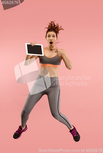 Image of Image of young woman over blue background using laptop computer or tablet gadget while jumping.