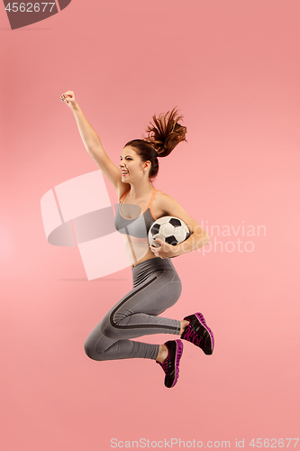 Image of Forward to the victory.The young woman as soccer football player jumping and kicking the ball at studio on a red