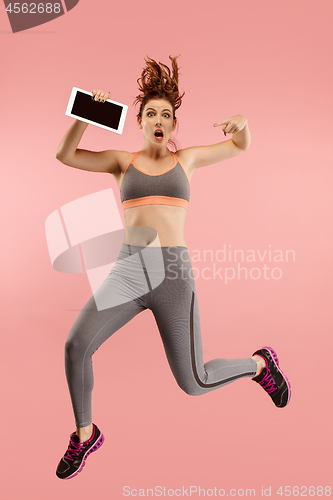 Image of Image of young woman over blue background using laptop computer or tablet gadget while jumping.