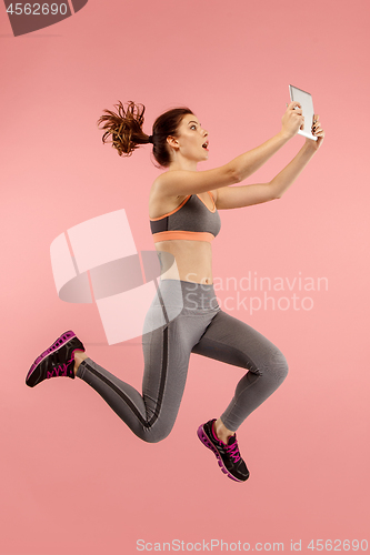 Image of Image of young woman over blue background using laptop computer or tablet gadget while jumping.