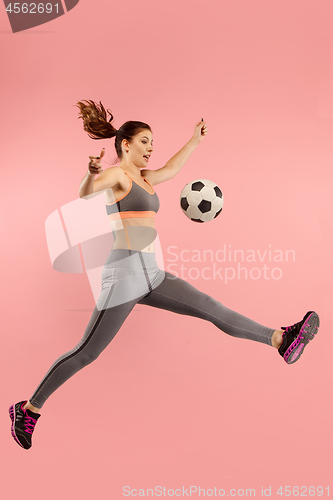 Image of Forward to the victory.The young woman as soccer football player jumping and kicking the ball at studio on a red