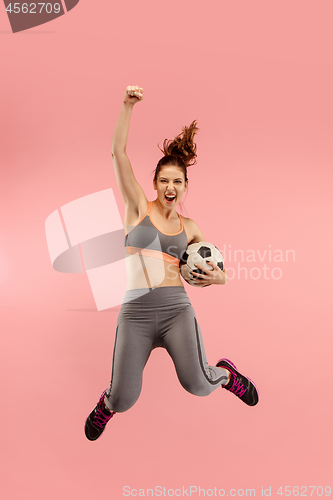 Image of Forward to the victory.The young woman as soccer football player jumping and kicking the ball at studio on a red