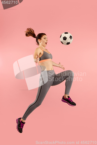 Image of Forward to the victory.The young woman as soccer football player jumping and kicking the ball at studio on a red