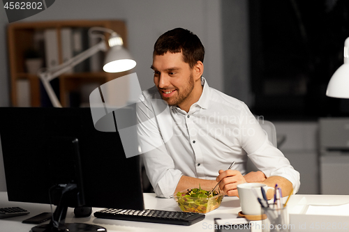 Image of businessman at computer eating at night office