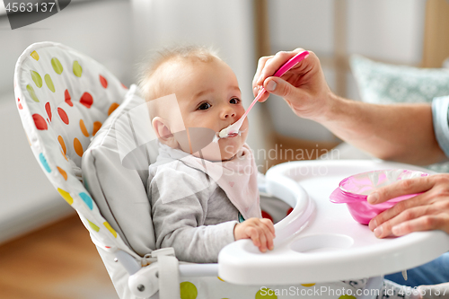 Image of father feeding baby sitting in highchair at home