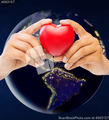 Image of hands holding red heart over earth in space