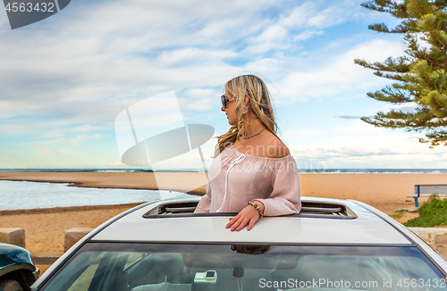 Image of Road trip to beach. Carefree woman in sunroof with views