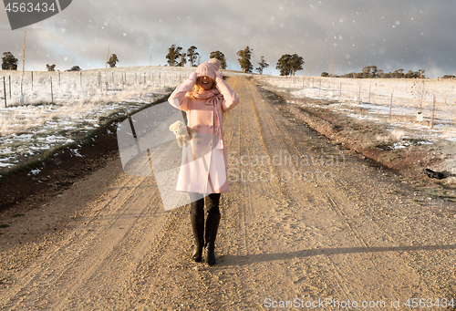 Image of Happy go lucky woman walking down dirt road in light snow fall