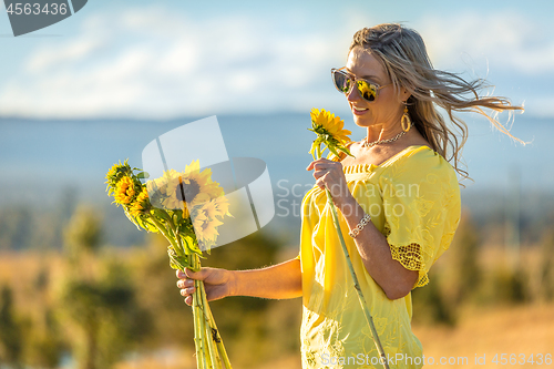 Image of Happy woman holding sunflowers hair blowing in the wind
