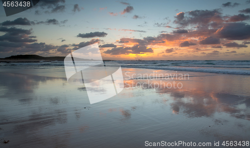 Image of Mirrored coastal reflections in wet beach sand at sunrise