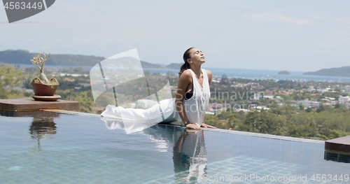 Image of Relaxed woman doing baby cobra exercise near swimming pool against beautiful scenery