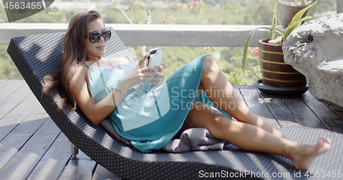 Image of Attractive woman with smartphone resting on chaise lounge