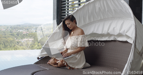 Image of Adult barefooted woman using laptop on balcony against landscape at tropical resort