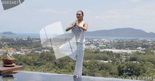 Image of Adult woman practicing yoga in poolside against amazing landscape