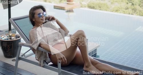 Image of Woman relaxing on deckchair beside swimming pool enjoying vacation time