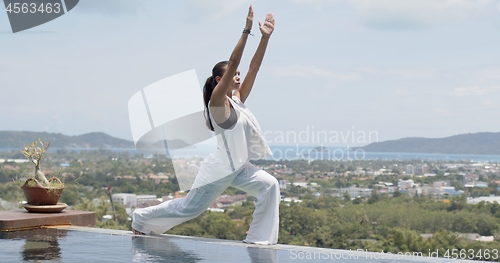 Image of Adult woman doing balancing exercise poolside against amazing landscape of resort on sea shore