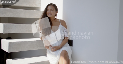 Image of Happy young woman sitting on stairs and looking away