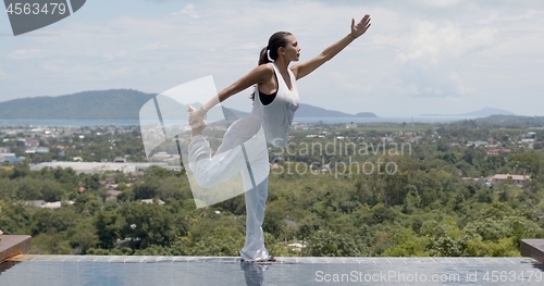 Image of Barefooted woman in standing bow pose near swimming pool against green forested islands