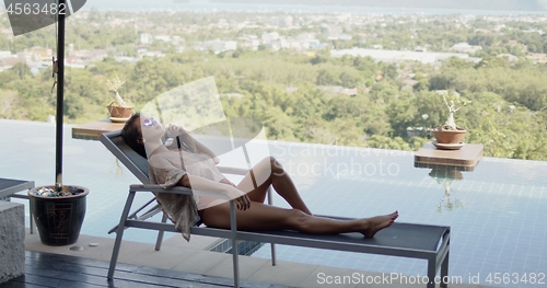 Image of Woman lying on deckchair on top of hotel pool terrace