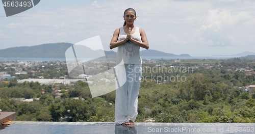 Image of Woman meditating while standing poolside against tropical coast