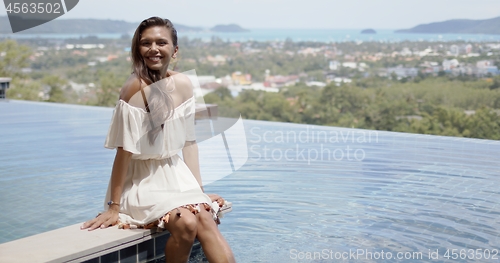 Image of Happy relaxed woman sitting poolside against ocean coast