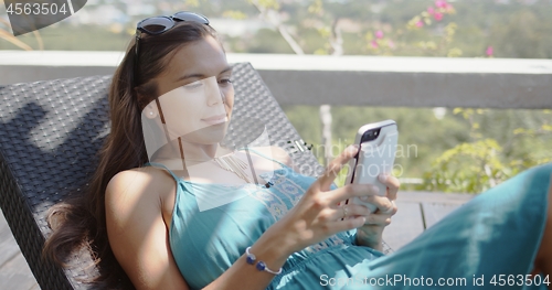 Image of Relaxed woman sitting on lounge chair and using smartphone